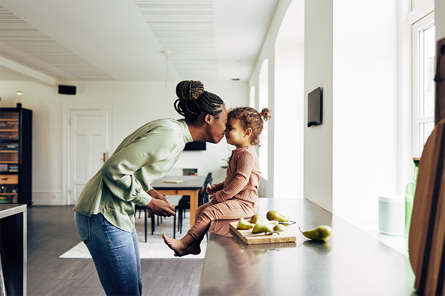 Personal Insurance - Young Mother Standing in the Kitchen Having Fun with Her Daughter as She Prepares Her a Snack
