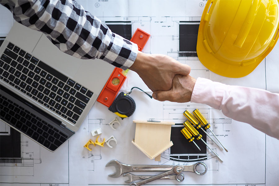 Specialized Business Insurance - Closeup Portrait of Two Contractors Shaking Hands Over a Table with Blueprints and Construction Tools